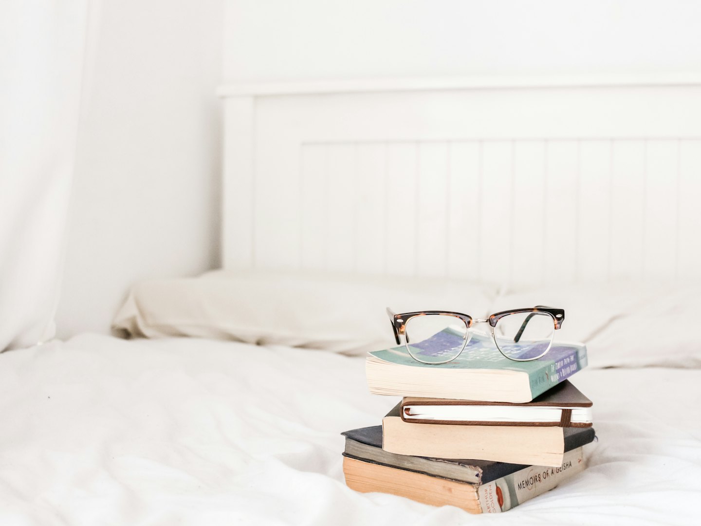 Bücherstapel mit Lesebrille auf einem weißen Bett.