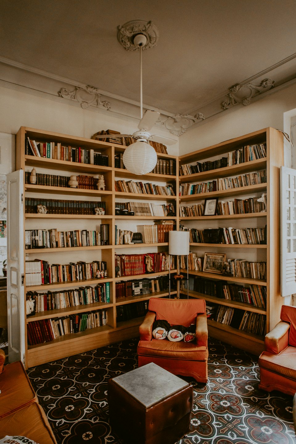 Gemütlicher Leseraum mit zwei großen Bücherregalen und einem orangefarbenen Sessel.